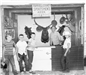 Historic photo of four boys standing in front of hunters booth.