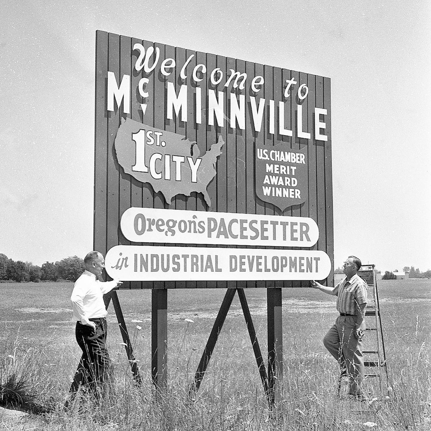 2 men standing by large Welcome to McMinnville sign.